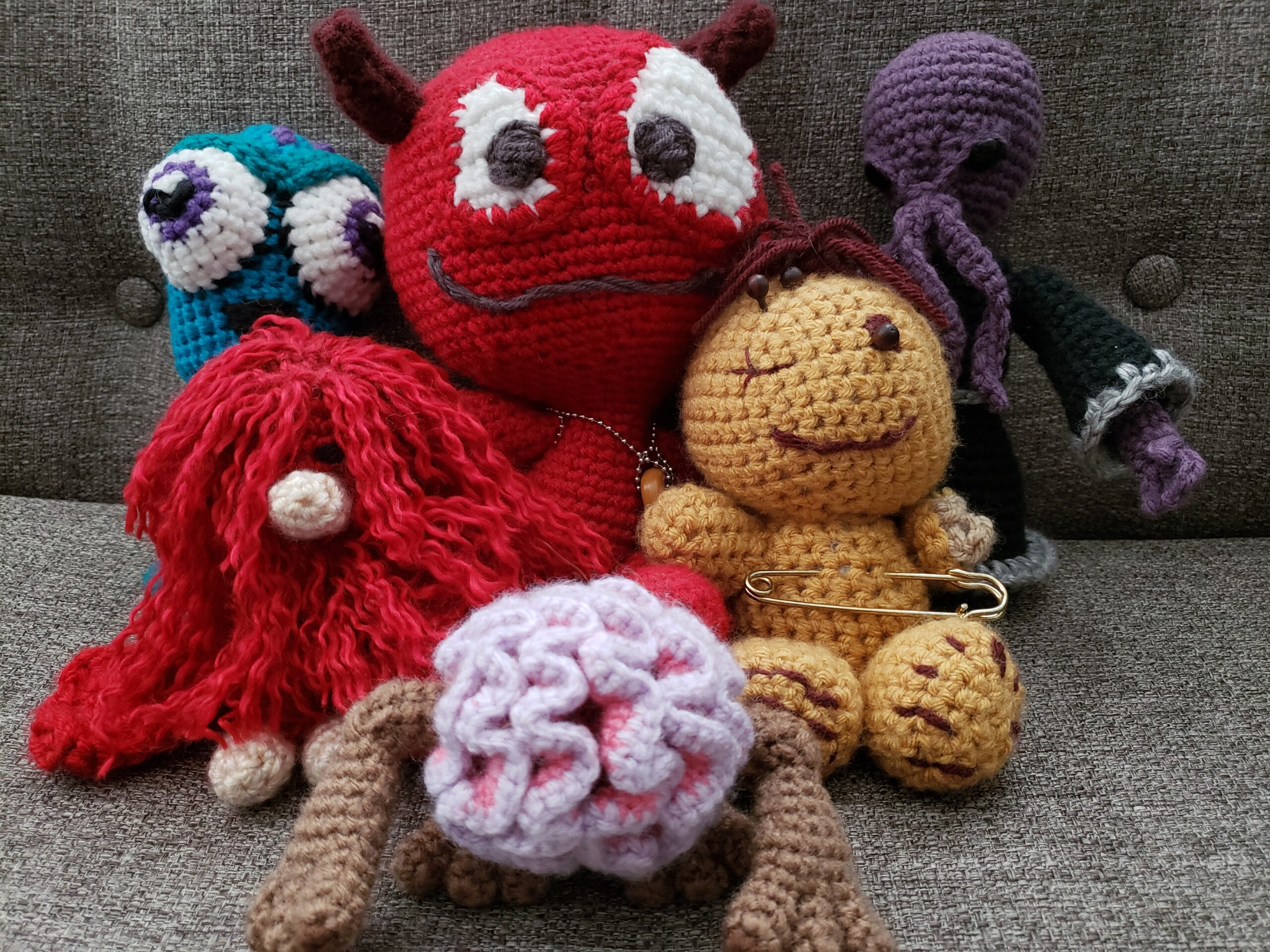 Several different crocheted amigurumi: a squid, a red yeti, a demon named Stinky, an ilithid, a voodoo doll, and an intelligence devourer