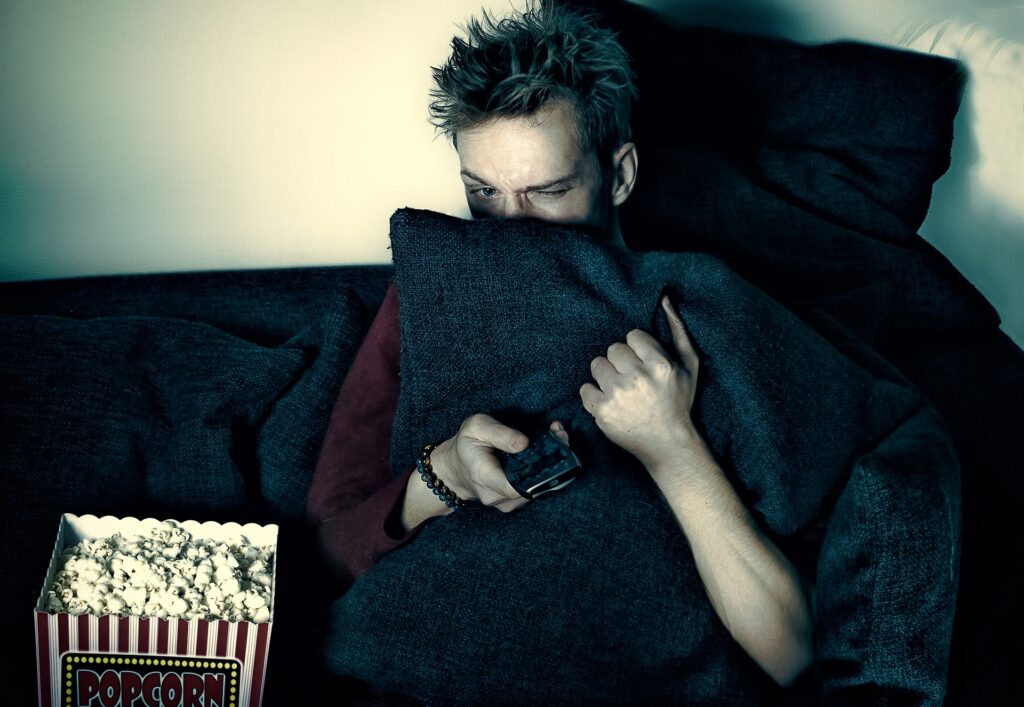 Man hiding behind pillow watching scary movie