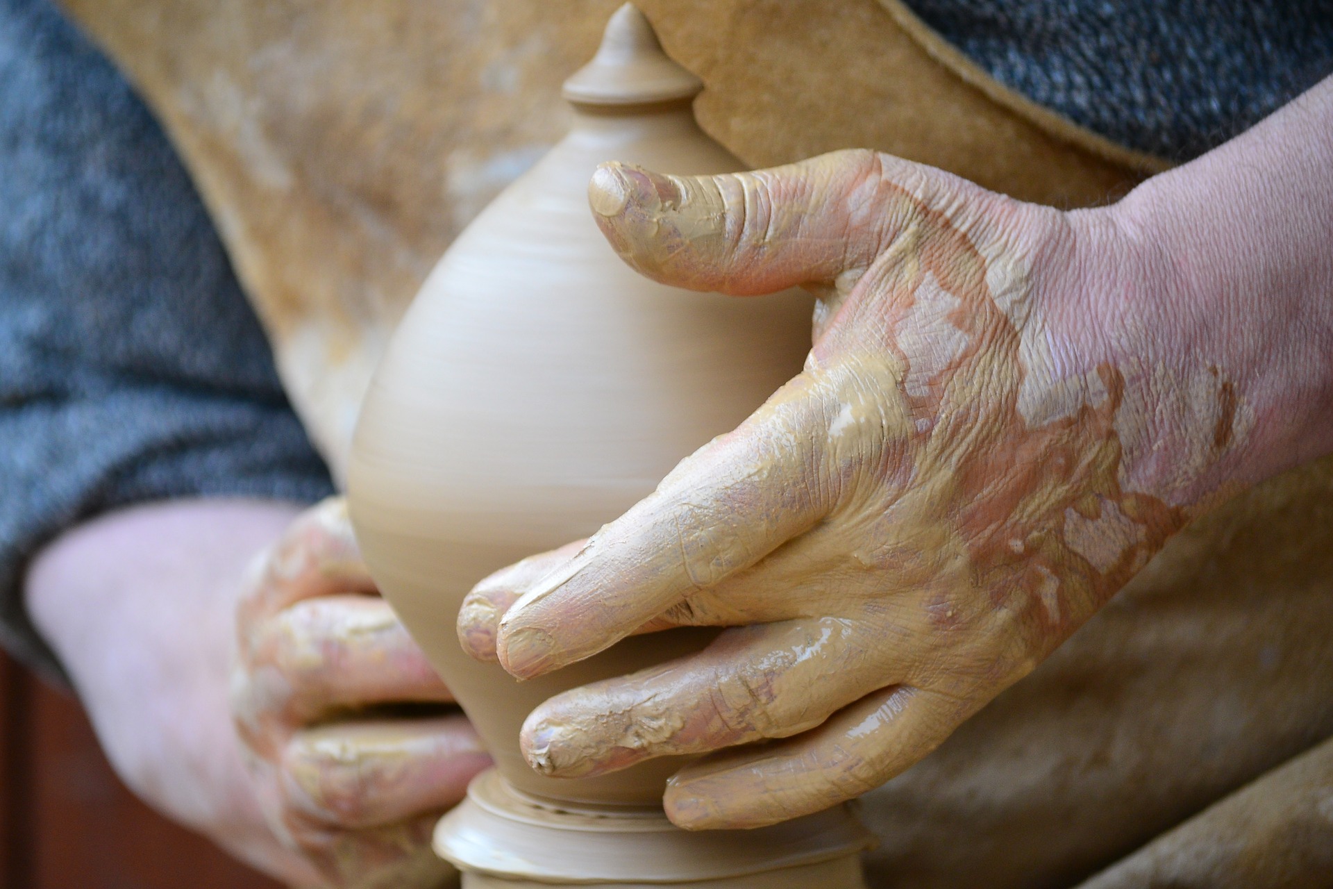 a man's muddy hands around a nearly finished pot on a wheel